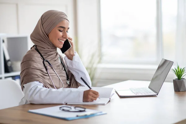 Başörtülü doktor telefonda konuşuyor ve notlar alıyor. — Stok fotoğraf