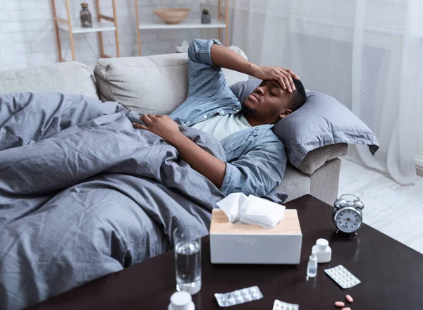Malato nero uomo avendo febbre sdraiato su divano a casa — Foto Stock