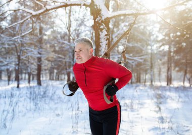 İşlevsel eğitim. Kış aylarında kışın karlı parkta TRX spor kemerleriyle egzersiz yapan yaşlı adamın portresi.