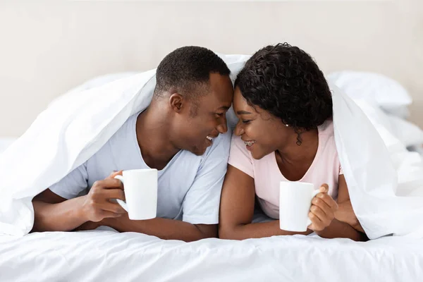 Romántica pareja negra tendida debajo de una manta, bebiendo té — Foto de Stock