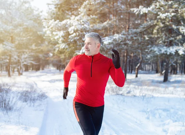 Soğuk hava koşusu konsepti. Karlı kış parkında spor kıyafetleri içinde koşan formda bir adam. Mevsimlik çalışma