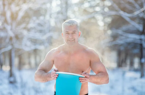 Красивый пожилой мужчина с обнаженной грудью держит ведро холодной воды на открытом воздухе зимой. Концепция акклиматизации — стоковое фото