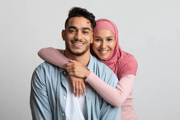 Porträt eines muslimischen Paares, das sich vor grauem Hintergrund umarmt und in die Kamera lächelt — Stockfoto