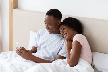 Afro-Amerikan çiftleri seviyorlar. Akıllı telefondan birlikte fotoğraf izliyorlar.