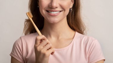 Çevre dostu bambu diş fırçası tutan, diş temizleyen genç ve mutlu bir kadın.