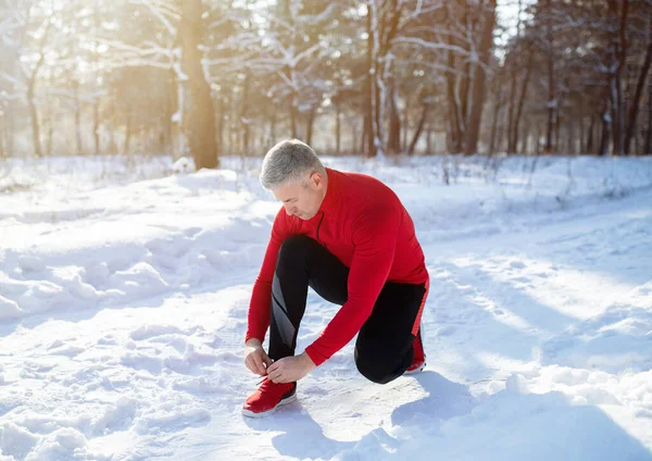 Matura jogger în cald sport îmbrăcăminte leagă șireturi pe drum de zăpadă la parc de iarnă — Fotografie, imagine de stoc