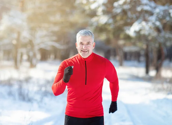 冬にはクロスカントリーが行われる。幸せなフィットシニア男ジョギングで雪の森で晴れた日の朝 — ストック写真