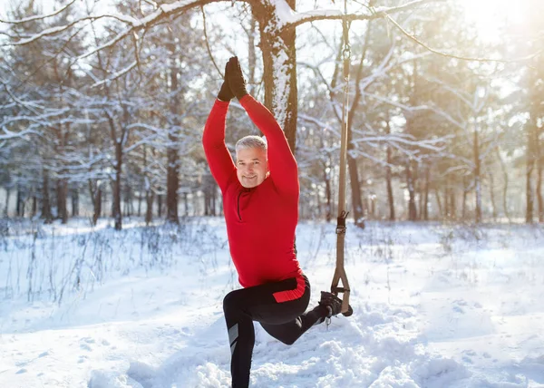 Concepto de fitness de invierno al aire libre. Entrenamiento de hombre mayor deportivo con correas de resistencia TRX en bosque nevado —  Fotos de Stock