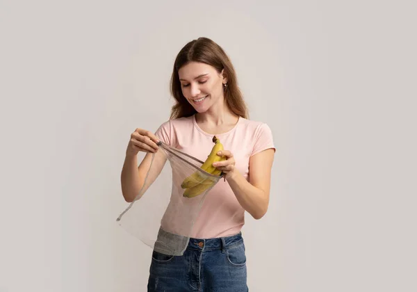 Shopping senza sprechi. felice Millennial donna mettendo banane in riutilizzabile stringa borsa — Foto Stock