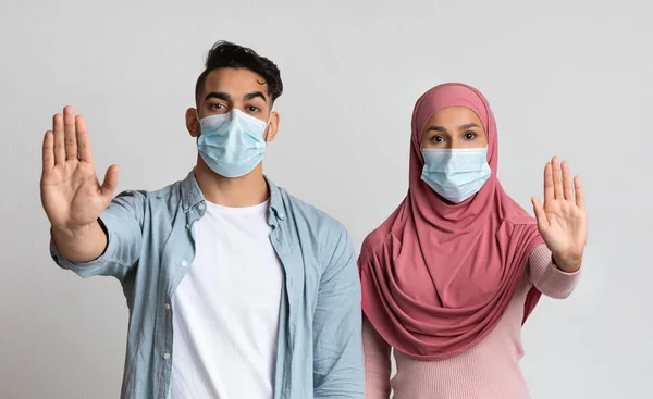严重的穆斯林夫妇在医疗面具展示停止手势与开放手掌 — 图库照片