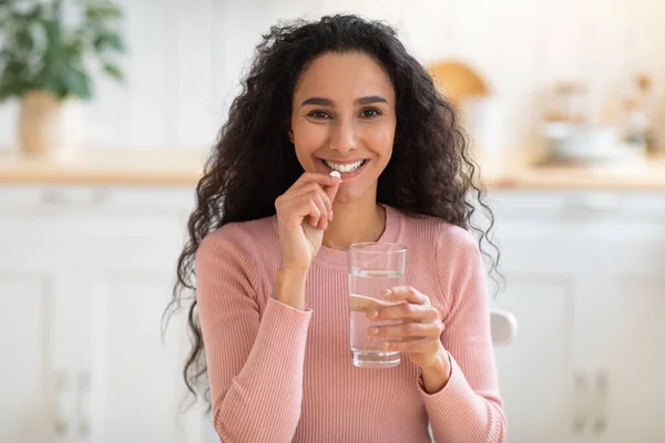 Integratore di bellezza. Sorridente bruna donna che prende la pillola di vitamina e beve acqua — Foto Stock