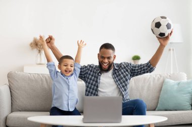 Afrikalı Baba ve Oğlu içeride dizüstü bilgisayarda futbol izliyorlar.