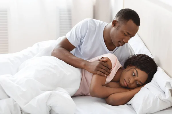 African guy touching his upset woman, laying in bed — Stock Photo, Image