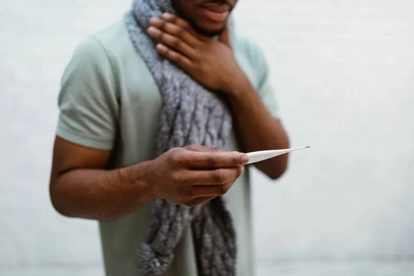 Больной африканский человек держит термометр, стоящий на сером фоне, обрезанный — стоковое фото