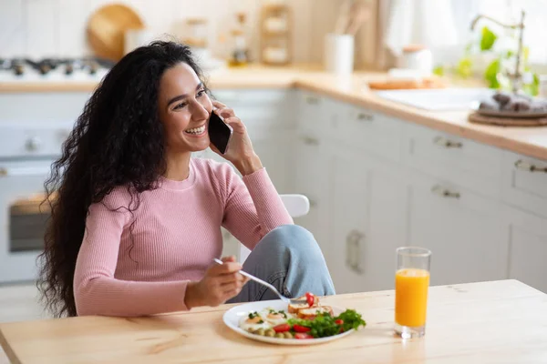 Cheerful Brunette Woman Talking On Mobile Phone And Eating Breakfast In Kitchen — Stock Photo, Image