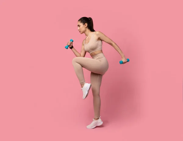 Junge Frau übt mit Hanteln auf pastellfarbenem Hintergrund — Stockfoto