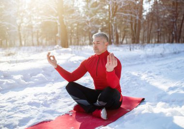 Açık havada kış yogası konsepti. Nilüfer çiçekli poz veren huzurlu olgun bir adam, karlı parkta gözleri kapalı meditasyon yapıyor.