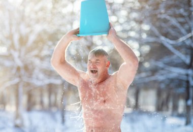 Senior man tempering his body, developing resistance to cold, pouring water onto himself outdoors in winter park clipart