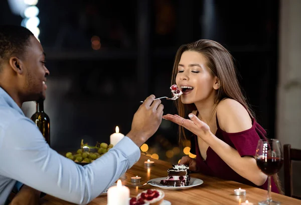 Casal misto alimentando uns aos outros com sobremesa na data romântica no restaurante — Fotografia de Stock