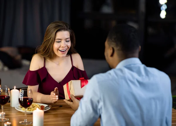 Czarny człowiek zaskakujące jego dziewczyna z darem podczas romantycznej kolacji w restauracji — Zdjęcie stockowe
