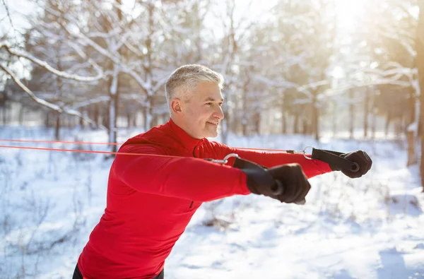 Kış parkında süspansiyon kayışlarıyla antrenman yapan atletik olgun adam.