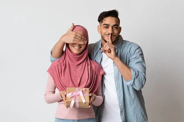 Surprise Present. Loving arab man covering muslim girlfriends eyes and giving gift — Stock Fotó