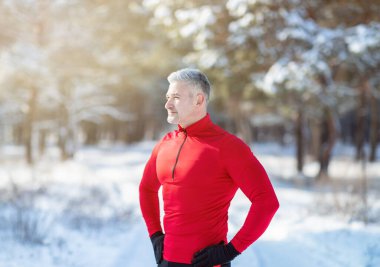 Spor giyim sektöründe sportif olgun bir adam karlı parkta kış antrenmanı yaparken mola veriyor. Sezonluk spor konsepti