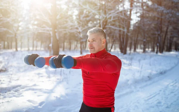 Outdoor bodybuilding strength workout. Senior man exercising with dumbbells, pumping up muscles at snowy park, panorama — Stock Photo, Image
