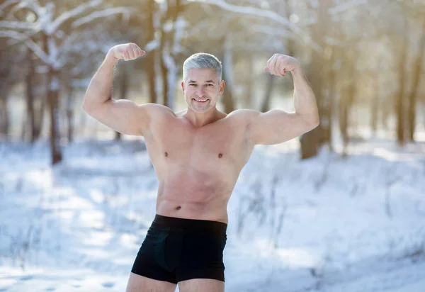 Bonito homem sênior com tronco nu mostrando seus bíceps fortes na geada de inverno na floresta nevada. Conceito de aclimatação — Fotografia de Stock