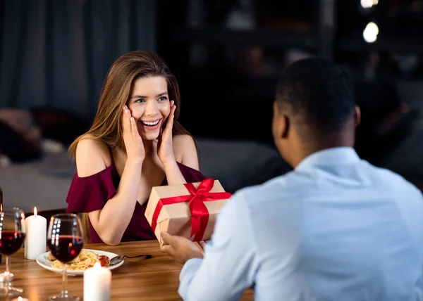 Cadeau voor jou. Romantische zwarte man maken verrassing voor vriendin in restaurant — Stockfoto