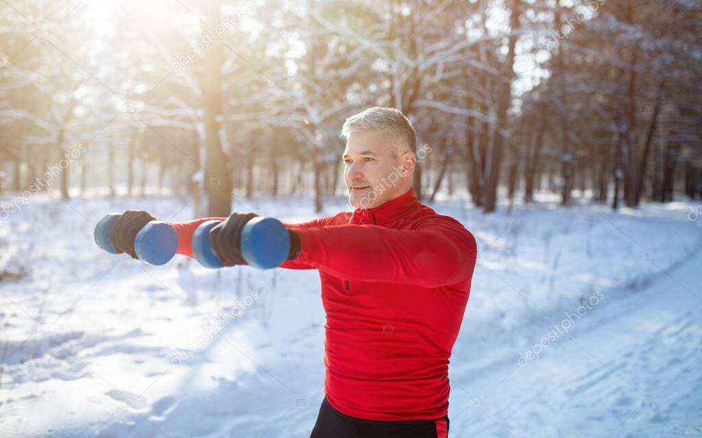 Outdoor bodybuilding strength workout. Senior man exercising with dumbbells, pumping up muscles at snowy park, panorama