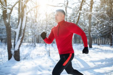 Senior athletic man in sportswear running at winter park, copy space. Seasonal outdoor sports and cold tempering concept clipart