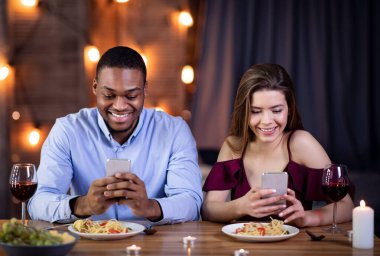 Sürtünme. Restoranda akıllı telefonlarına bakan ırklar arası genç bir çift.