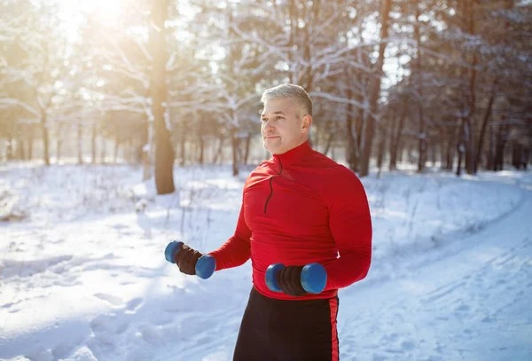 Conceptul sporturilor de iarnă. Un bătrân puternic care lucrează cu gantere, antrenându-şi muşchii în parcul de zăpadă. — Fotografie, imagine de stoc