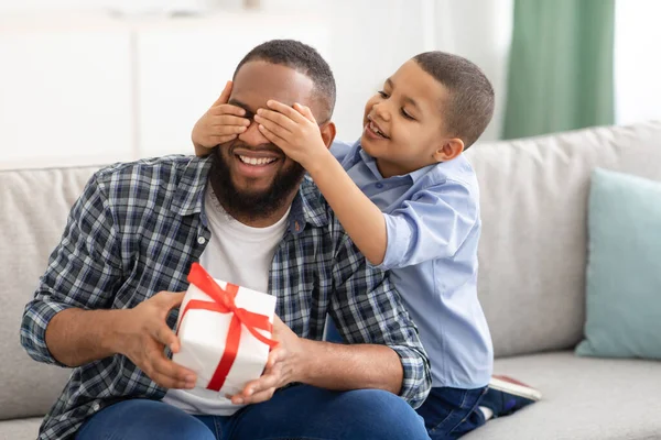 Little Son Gratulerar Black Fader Ge inslagen gåva Inomhus — Stockfoto