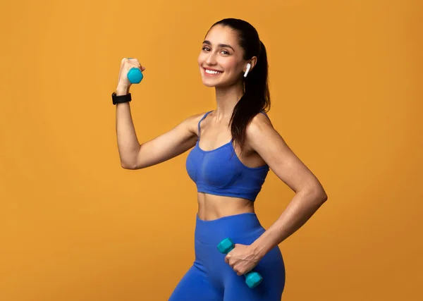 Sorrindo Sporty mulher posando com halteres isolados em fundo laranja — Fotografia de Stock