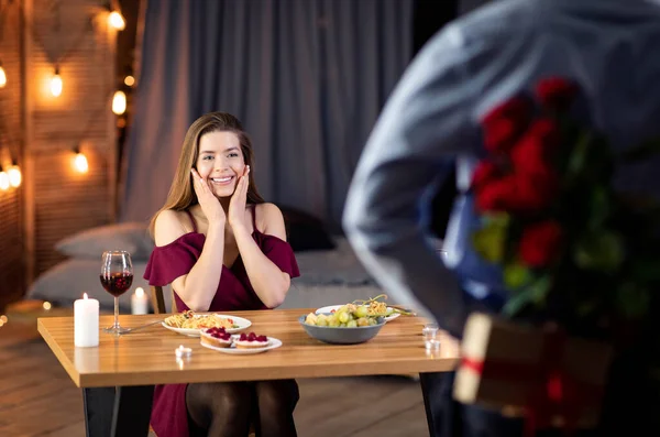 Amante homem surpreendente namorada com rosas vermelhas na data romântica no restaurante — Fotografia de Stock
