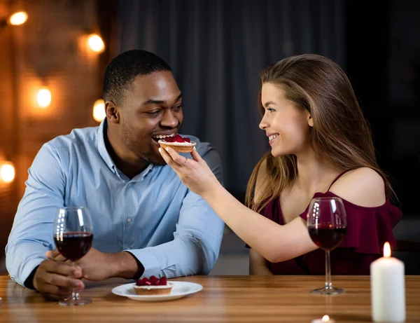 Romantyczna para międzyrasowa je kolację w restauracji, karmi się nawzajem — Zdjęcie stockowe