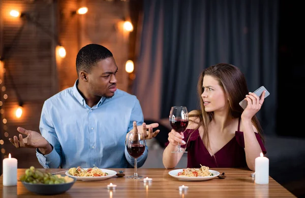 Geïrriteerde zwarte man ruziën met zijn vriendin bezig met mobiele telefoon op datum — Stockfoto