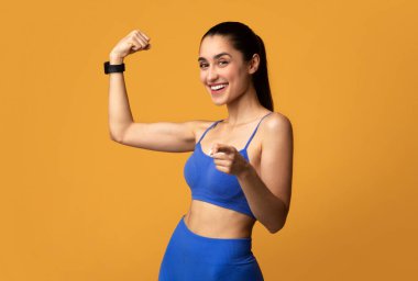 Bisepslerini gösteren ve kamerayı gösteren mutlu bir kadın.