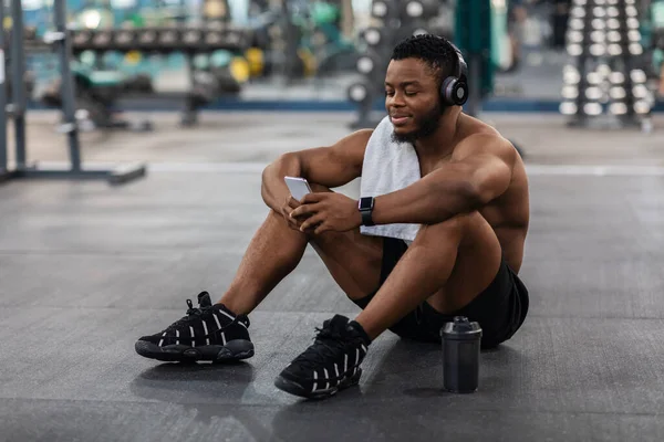 Avslappnad idrottsman lyssnar på musik på mobiltelefon, gym interiör — Stockfoto