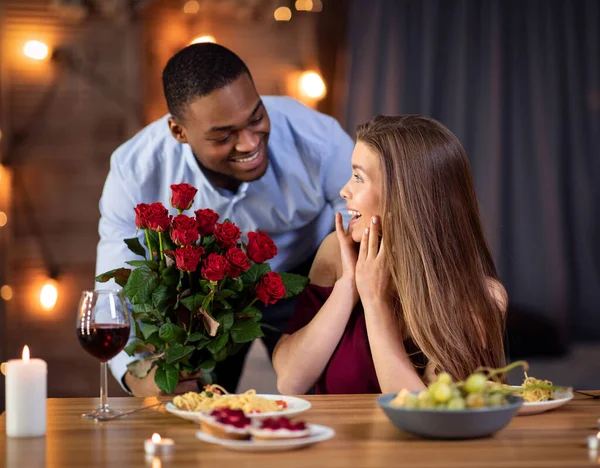Valentijnsdag verrassing. Elegante Afrikaanse man geeft rozen aan vriendin in restaurant — Stockfoto