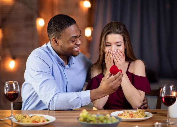 Bell'uomo africano che propone alla sua ragazza bianca di sposarlo al ristorante — Foto Stock