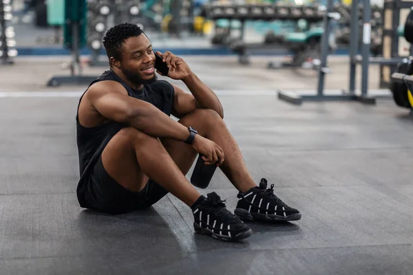 Schwarzer sitzt im Fitnessstudio auf dem Fußboden und telefoniert — Stockfoto