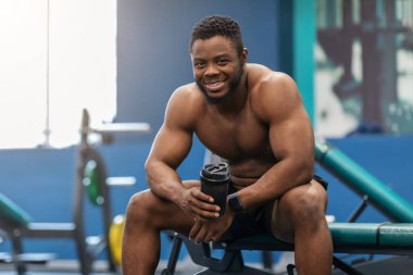 Gülümseyen Afro-Amerikan tişörtsüz vücut geliştirici Protein içiyor
