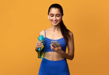 Akıllı telefon kullanan, elinde su şişesi olan sportif bir kadın.