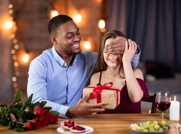 Любящий мужчина, закрывающий глаза девушкам и дарящий подарок на свидании в ресторане — стоковое фото