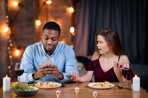 Έννοια Φάμπινγκ. Μαύρος απασχολημένος με Smartphone κατά τη διάρκεια του δείπνου με την κοπέλα του — Φωτογραφία Αρχείου
