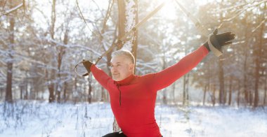 Total resistance fitness. Mature man working out with TRX system, training with suspension straps in snowy winter forest clipart