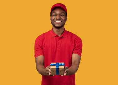 Siyah teslimatçı elinde hediye kutusuyla kameraya gösteriyor.